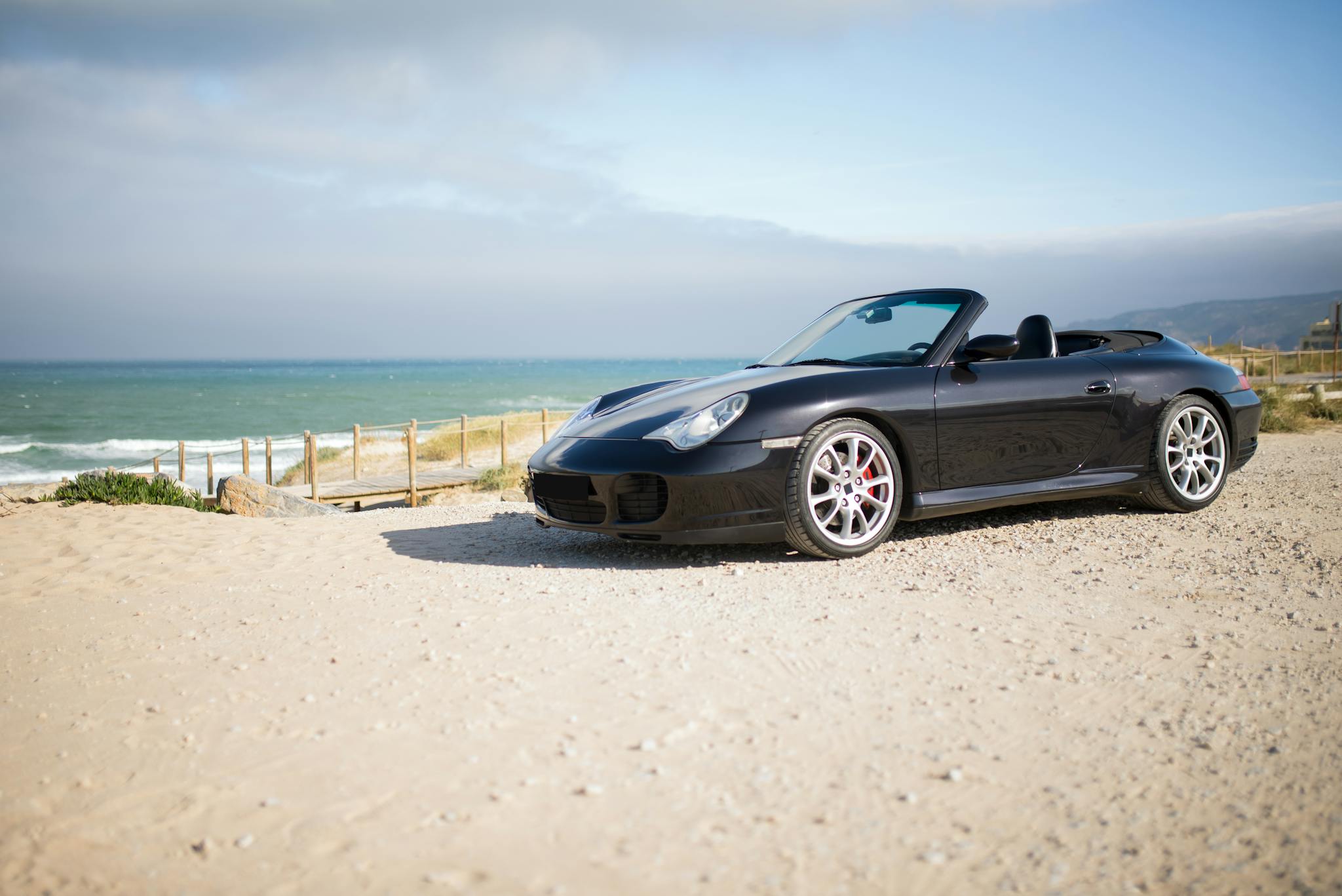 Elegant black convertible parked on a sunny beach in Portugal, offering a luxurious coastal vibe.
